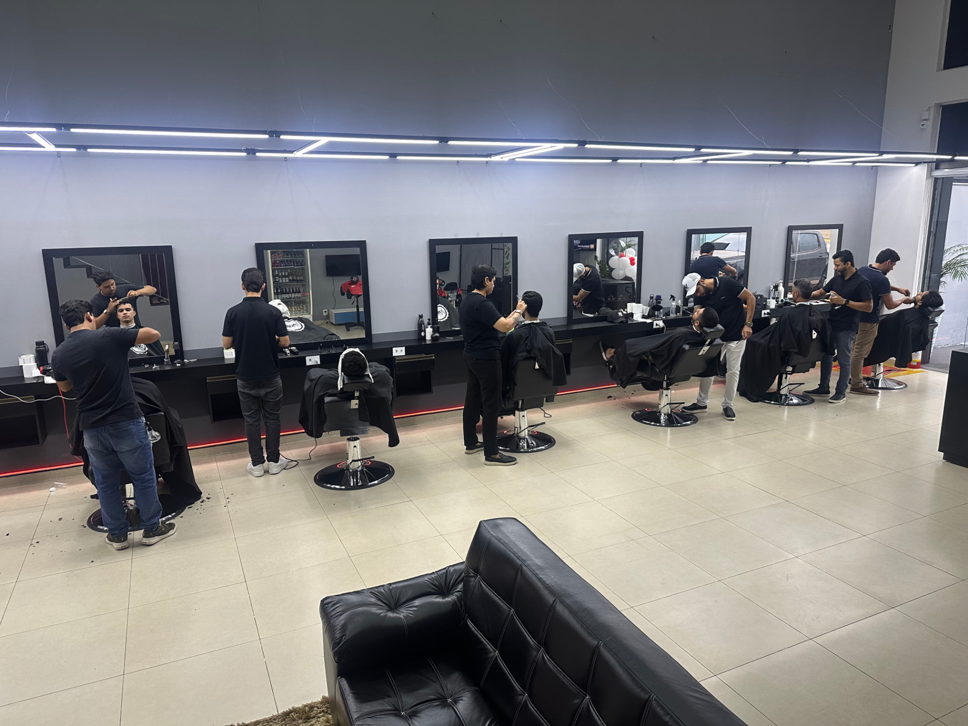 Interior da AUX Barbearia com estações de trabalho e barbeiros atendendo